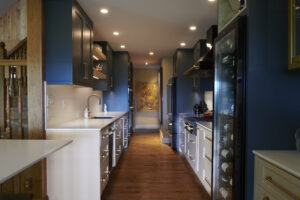 kitchen & bath remodeling in western north carolina: what high-end clients should know 1 a modern, mountain contemporary kitchen featuring dark blue cabinets, white countertops, and wood floors. a wine fridge stands to the right, with a colorful painting visible at the end of the galley kitchen.